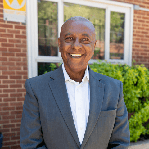 headshot of man standing in front of building 